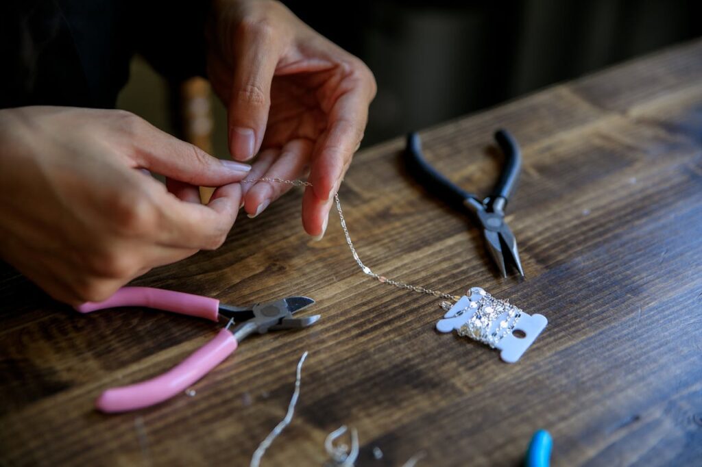 pexels-photo-10474333 Close-up of hands crafting jewelry with pliers and wire on a wooden table.