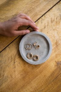 Top view of assorted gold earrings on a wooden surface with a hand reaching for them.